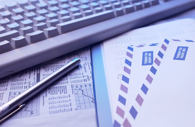 Close-up view of a silver pen, white keyboard, and some envelopes beside each other.