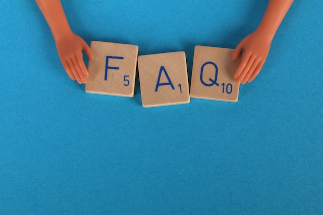 Uma foto em close de peças de Scrabble soletrando FAQ em uma superfície azul.