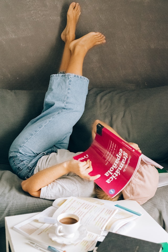 Mulher deitada de cabeça para baixo em um sofá lendo um livro sobre tradução de espanhol.