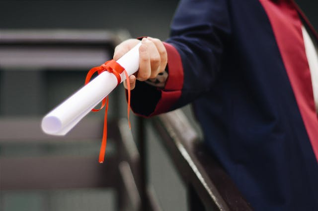 Uma foto de uma pessoa segurando um certificado dobrado e amarrado com uma fita.