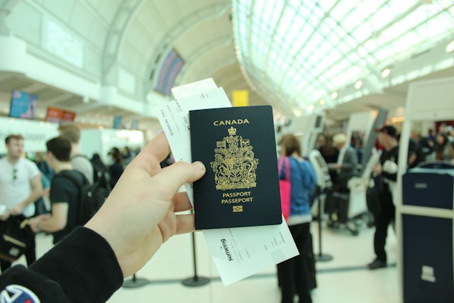 Uma pessoa está em um aeroporto movimentado e mostra seu passaporte canadense com um cartão de embarque.