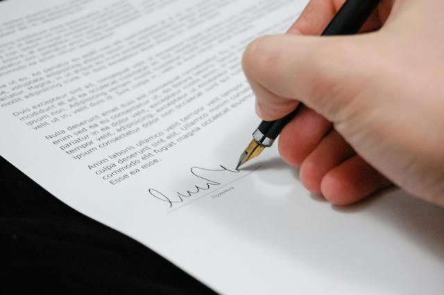 Uma foto de uma pessoa assinando um documento com uma caneta tinteiro.