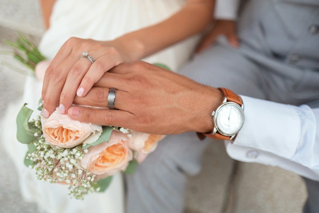 Um homem e uma mulher de mãos dadas enquanto exibem suas alianças de casamento.
