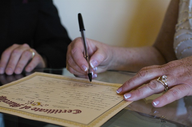 Foto de um casal assinando sua certidão de casamento no dia do casamento. 
