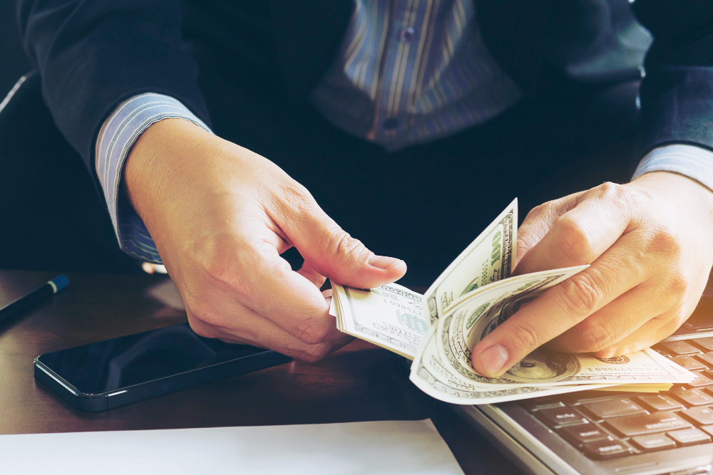 Uma pessoa conta cédulas de dólar em um teclado de computador.