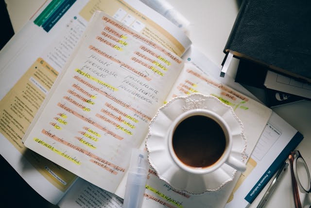 Uma xícara de café sobre um livro com anotações contendo palavras e suas traduções.