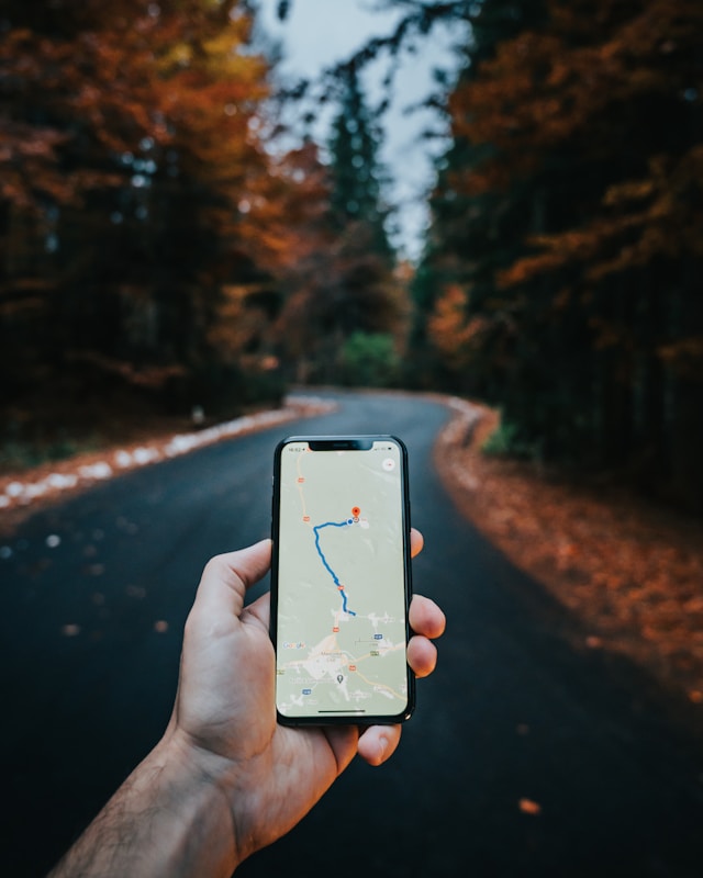 Uma pessoa em pé em uma estrada arborizada segurando um smartphone que exibe um mapa de navegação para um local ao norte.