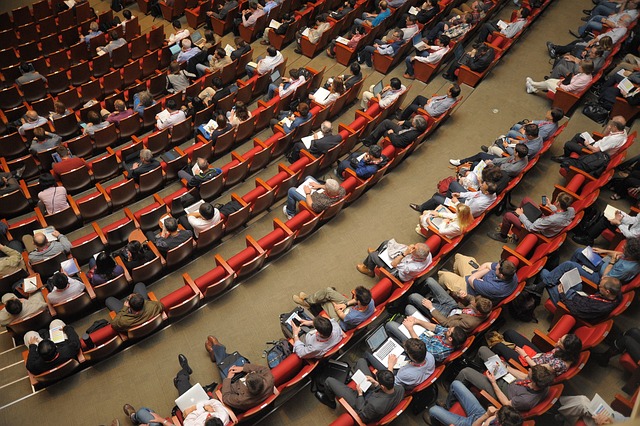 As pessoas se sentam em fileiras em um auditório.
