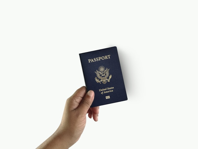 Uma mão segura o livreto do passaporte dos Estados Unidos em um fundo branco.
