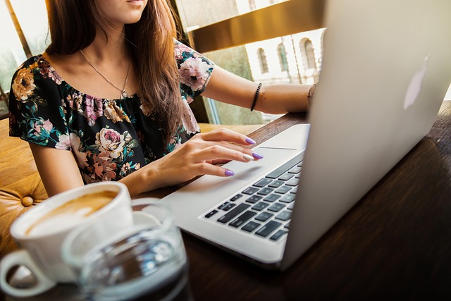 Uma pessoa usa um laptop prateado ao lado de uma caneca de café e um copo de água.
