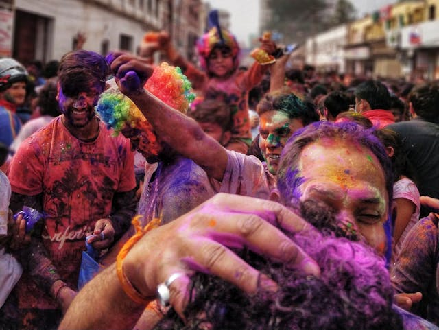 Pessoas cobertas com diferentes cores de tinta comemoram em público.