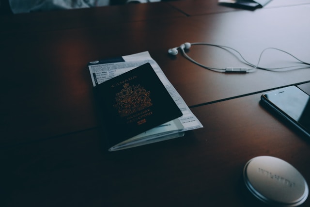 Um passaporte canadense em uma mesa ao lado de um telefone e um par de fones de ouvido com fio.