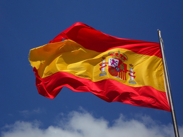 Uma bandeira espanhola em um mastro tremulando ao vento durante o dia.
