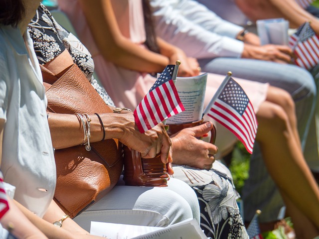 Algumas pessoas sentadas ao sol seguram mini bandeiras americanas.
