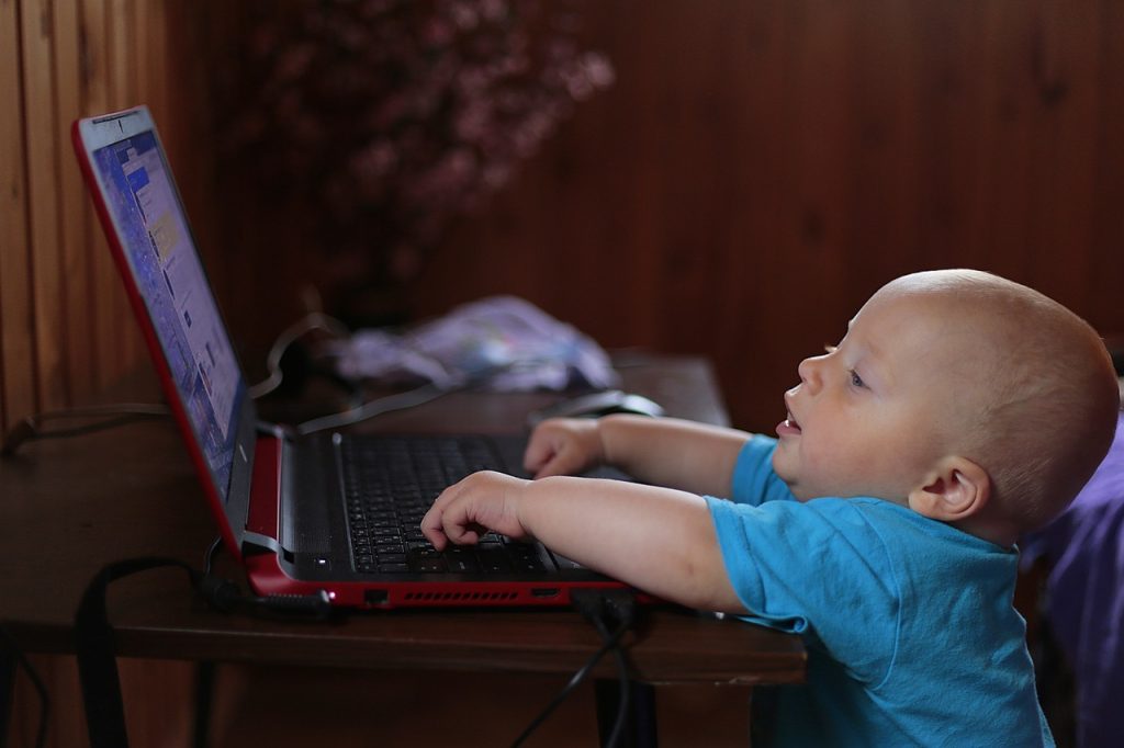 Uma criança coloca as mãos no teclado de um laptop aberto.
