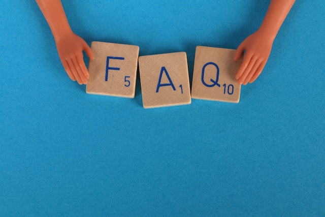 Eine Nahaufnahme von Scrabble-Kacheln, die auf einer blauen Fläche FAQ buchstabieren.