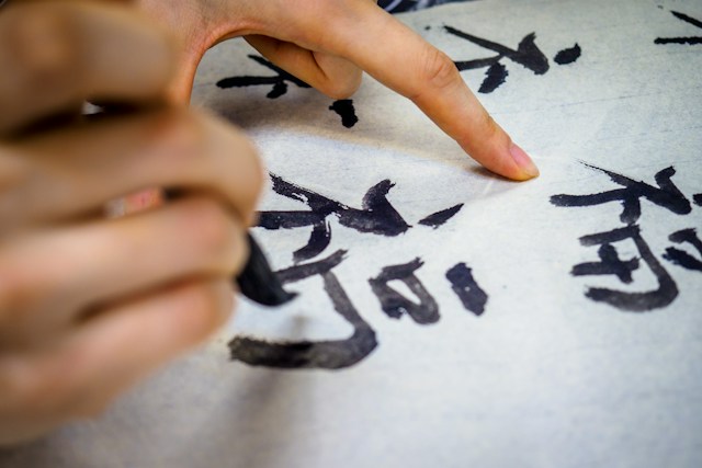 Eine Nahaufnahme einer Person, die mit schwarzer Tinte auf Chinesisch schreibt. 