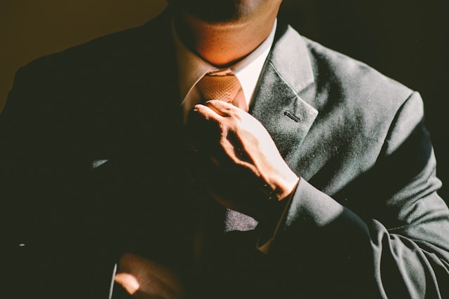 Ein Mann in einem schwarzen Anzug rückt seine braune Krawatte zurecht.
