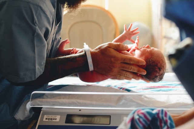 Eine Krankenschwester legt ein Neugeborenes auf eine Waage.
