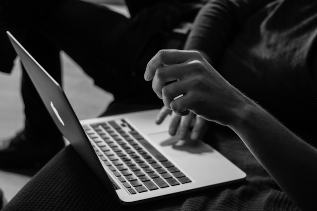 Eine Person benutzt ein MacBook, während andere im Hintergrund verweilen.
