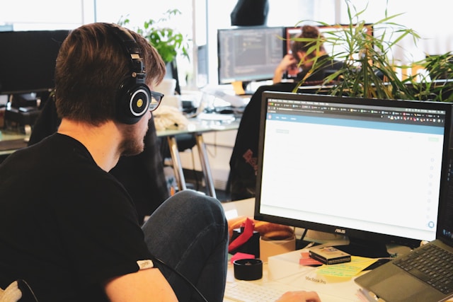 Eine Person mit schwarzen Kopfhörern benutzt einen Computer in einem Büro.