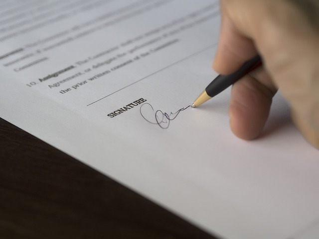 Eine Hand fügt eine Unterschrift auf einem gedruckten Dokument an.
