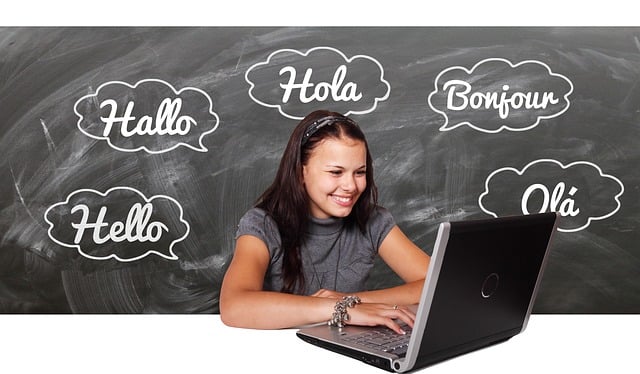 Eine Person benutzt einen Laptop vor einer Tafel, auf der das Wort "Hallo" in verschiedenen Sprachen steht.
