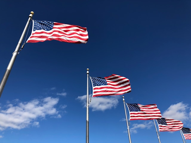 Drei U.S. Flaggen unter einem klaren blauen Himmel.
