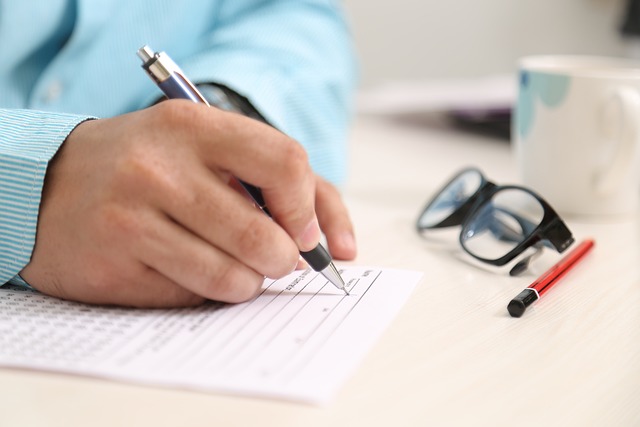 Eine Hand schreibt auf einem weißen Papier, daneben ein Bleistift und eine Brille.
H2: Wie man ein Dokument übersetzen lässt und 