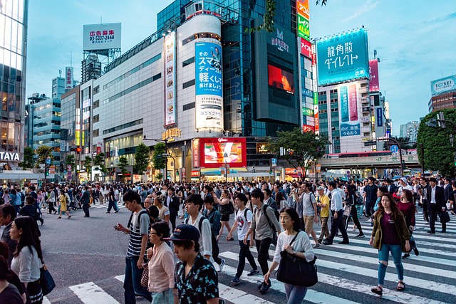 Menschen überqueren tagsüber einen Gehweg auf einer belebten japanischen Straße.
