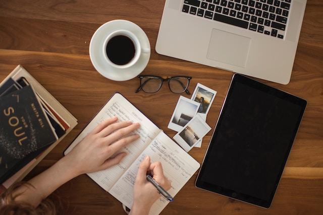 Un escritor escribiendo en un cuaderno junto a una taza de café