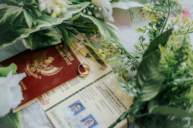 Una foto de documentos matrimoniales, un anillo y ramos de flores sobre una mesa.