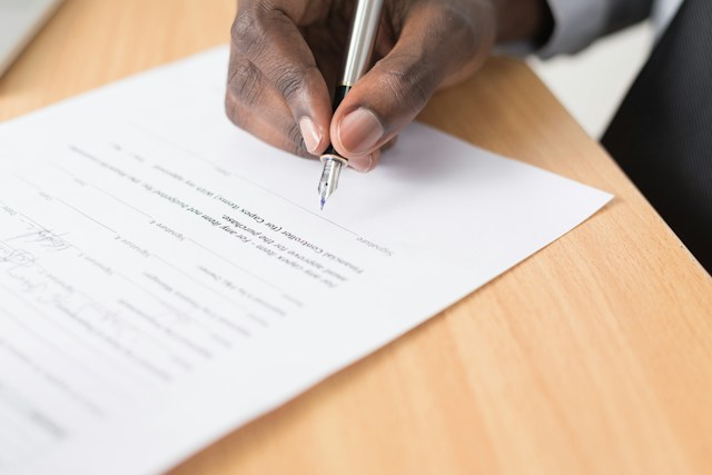 Una persona firma un documento oficial sobre una mesa de madera. 