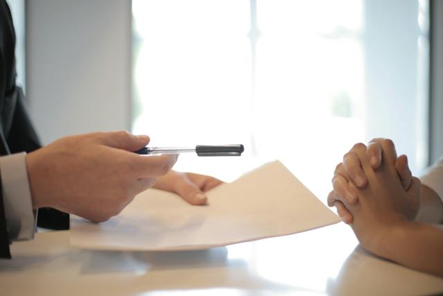 Una persona que entrega un bolígrafo y un documento a otra persona.
