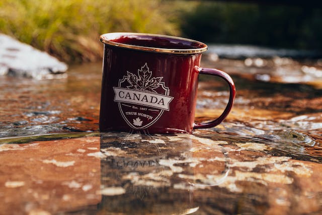 Una taza granate lleva escrito "Canadá" y una hoja de arce detrás del nombre del país.
