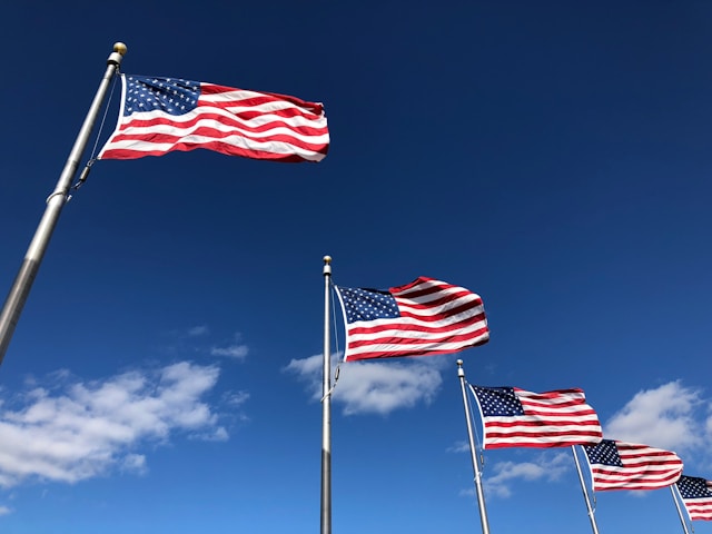 Tres banderas estadounidenses bajo un cielo azul despejado.
