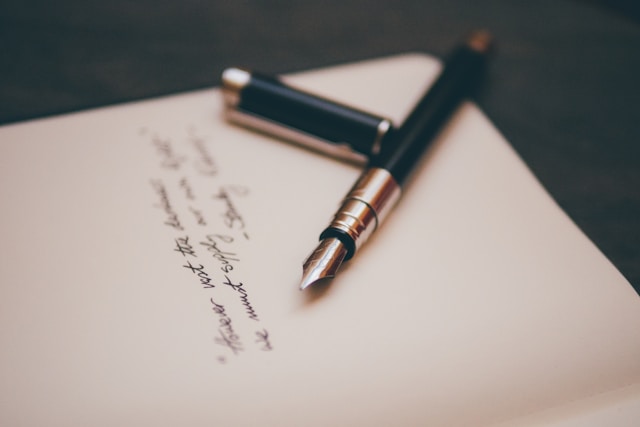 Una pluma estilográfica negra y plateada sobre un cuaderno con escritura negra.
