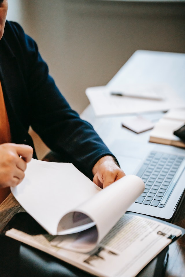 Personne feuilletant les pages d'un document sur un espace de travail en désordre.