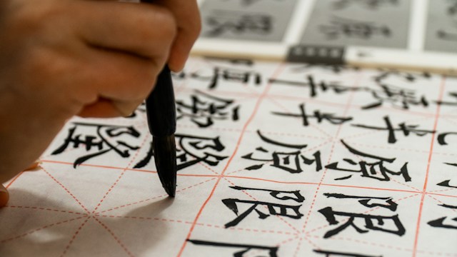 Photo d'une personne écrivant en chinois sur du papier.
