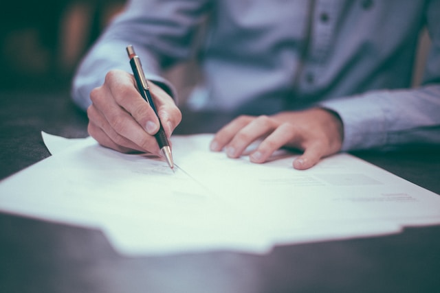 Photographie d'une personne écrivant sur des documents papier posés sur une table.