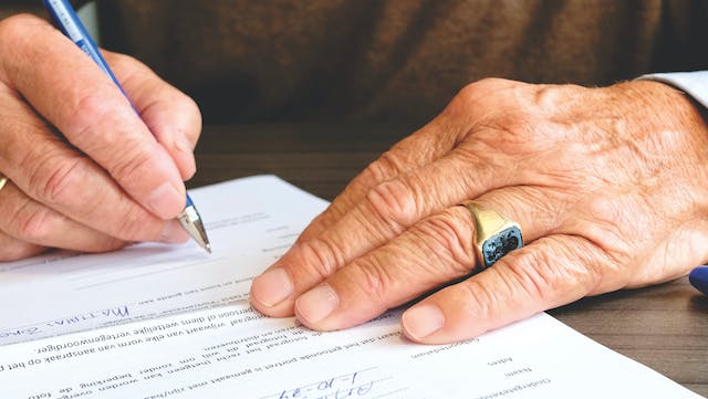 Une photo d'une personne portant une bague et signant un document.