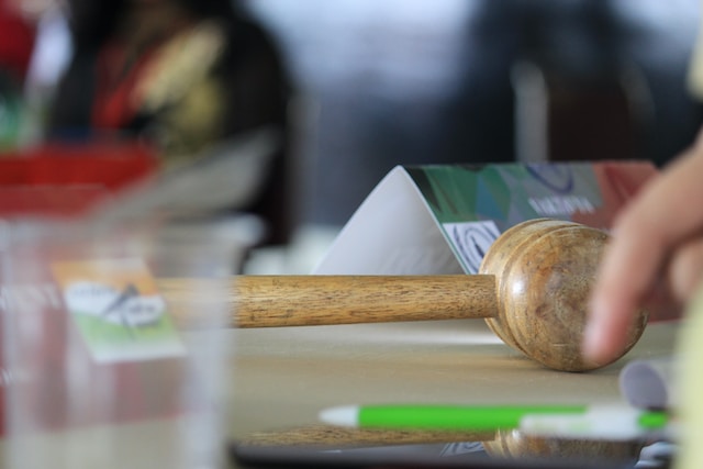 Une photo d'un marteau en bois et de quelques papiers sur un bureau.
