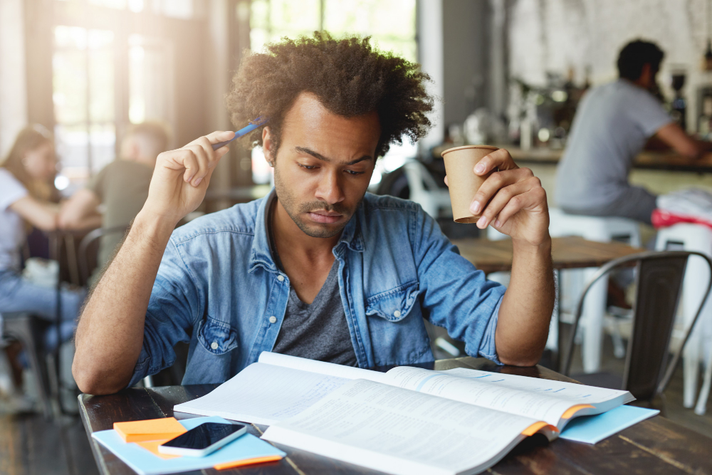 Une personne se gratte la tête avec un stylo et se concentre sur un livre.