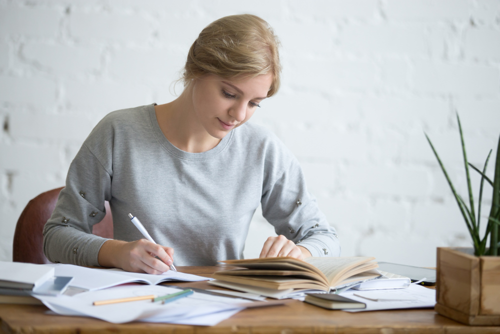 Une personne copie le texte d'un livre sur une feuille blanche.