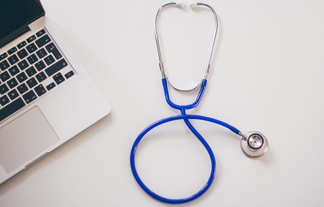 Un stéthoscope et un ordinateur portable argenté sur une surface blanche.
