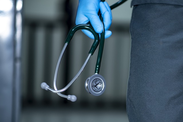 Une main gantée de bleu tient un stéthoscope.
