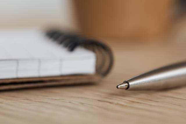 Un stylo en argent à côté d'un livre sur une surface en bois.
