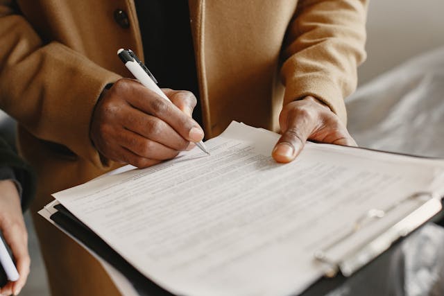 Une personne vêtue d'un manteau marron signe un document.