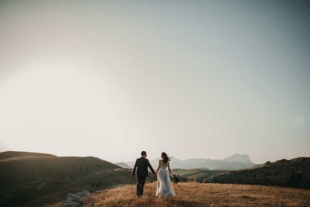 Una fotografia di una sposa e di uno sposo che camminano su una collina. 
