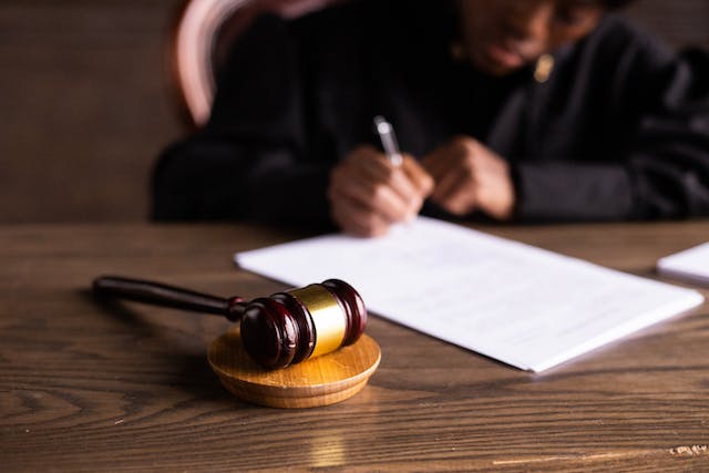 Una persona senza volto in veste di giudice che firma un documento su un tavolo con un martelletto.